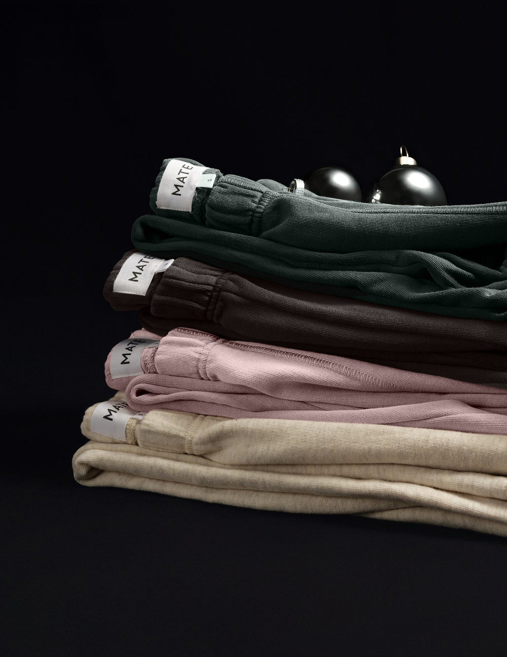 Folded organic pants stacked in green, brown, pink and cream beside silver ornaments – MATE the Label