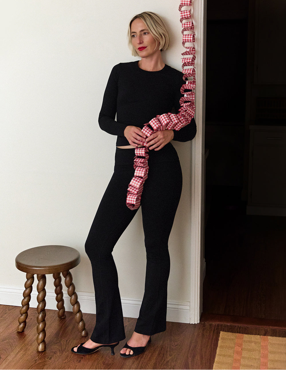 Woman in black organic stretch long sleeve top and flare pants holding a red gingham garland – MATE the Label