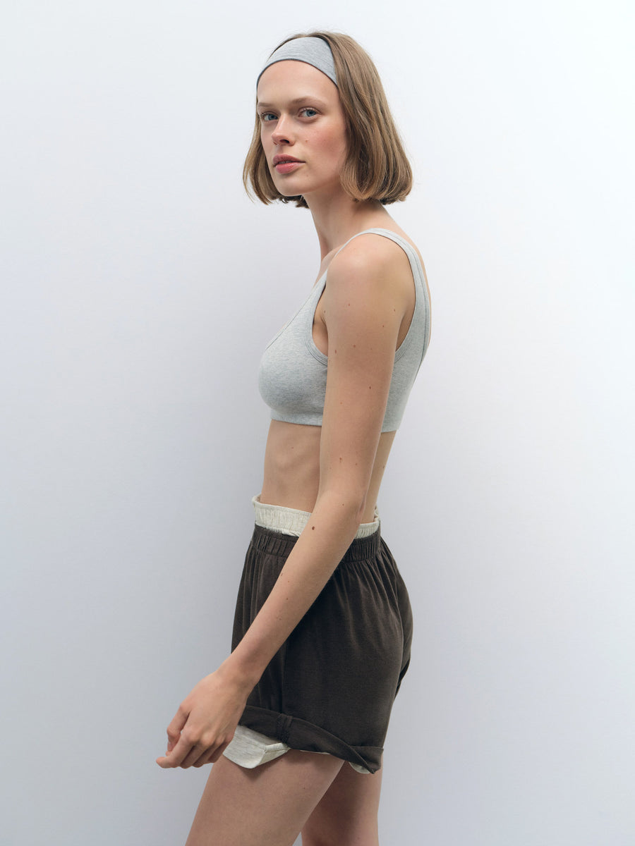 Woman wearing a light grey Organic Comfort Scoop Bralette with a matching headband and dark shorts.