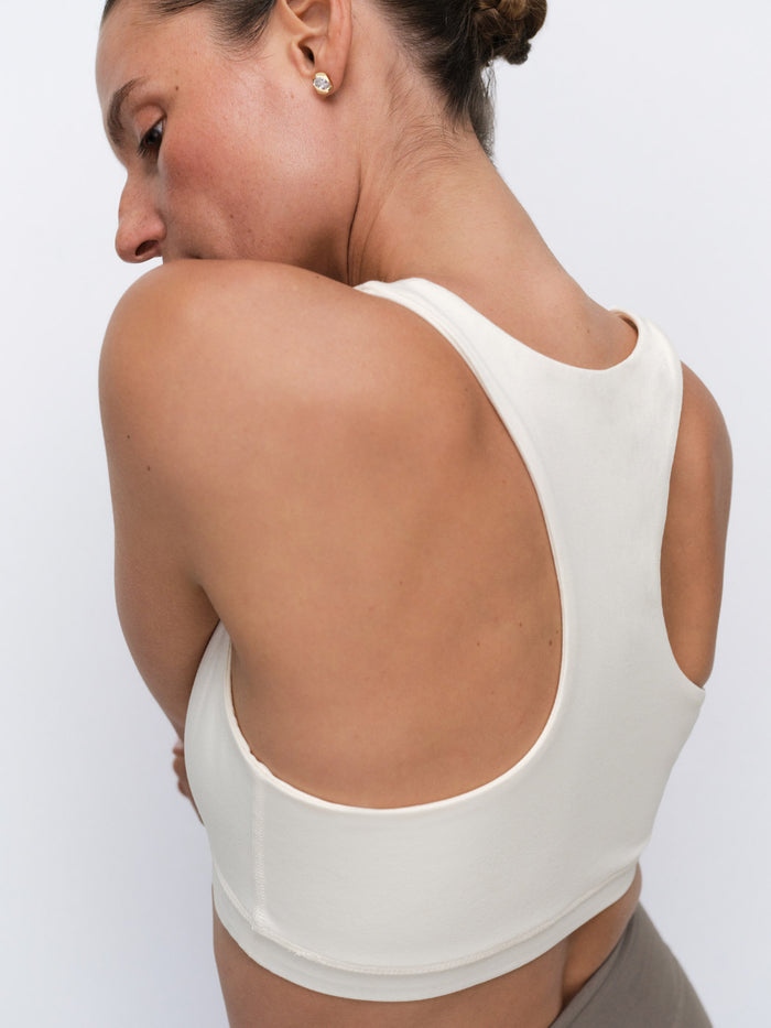 A woman shown from the back wearing a cream-colored athletic sports bra against a plain light gray background.