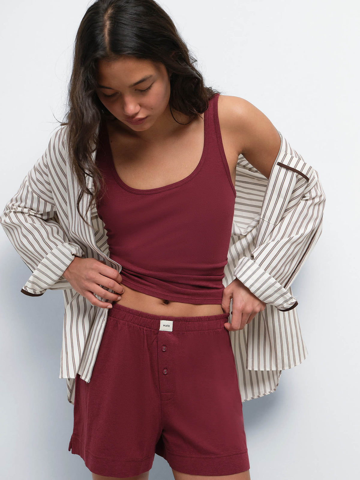 Model looking down with a striped shirt over the Tencel Sleep Scoop Tank in Garnet and matching shorts