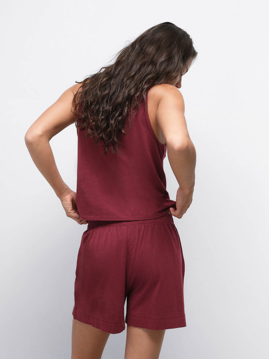 Back view of model with hands on hips wearing the Tencel Sleep Scoop Tank in Garnet with matching shorts