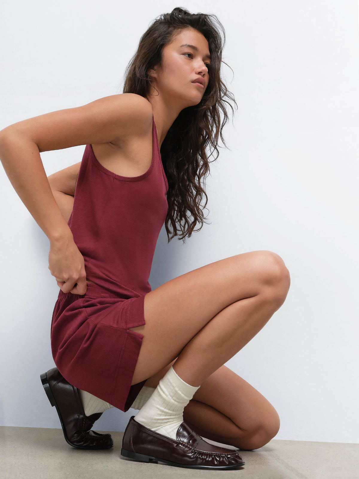 Model crouching with hand on hip in the Tencel Sleep Scoop Tank in Garnet and matching shorts
