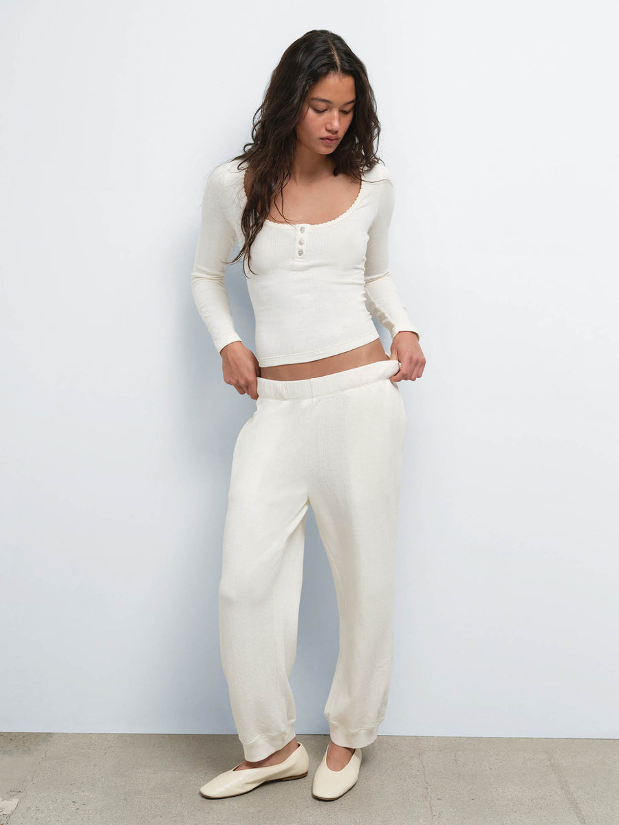 Full-length view of model with hands in pockets wearing the Organic Pointelle Henley and Jogger in Cream