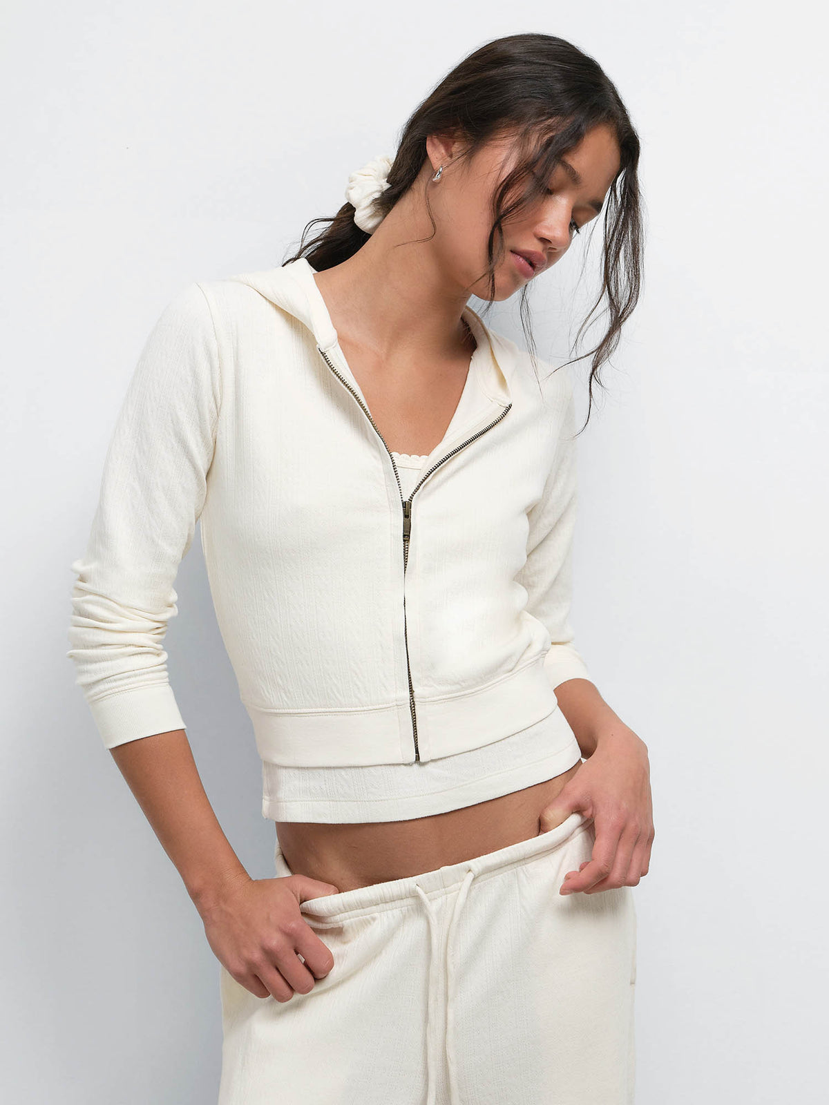Model looking down with a hand in her pocket, wearing the Organic Pointelle Shrunken Hoodie and Pant in Cream