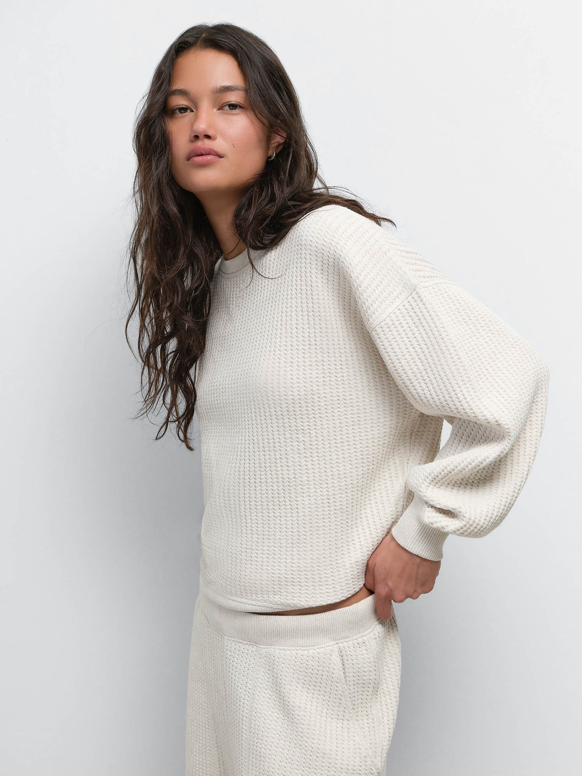 Model with hand on hip wearing the Organic Waffle Crewneck Sweatshirt and Sweatpant in Oat