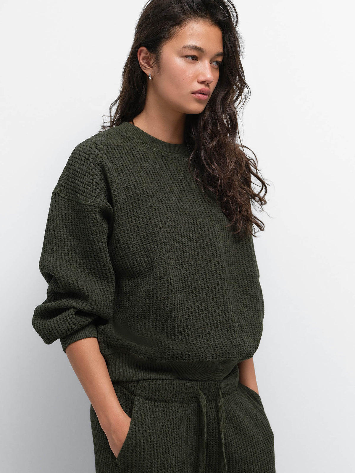 Three-quarter view of model with hands in pockets wearing the Organic Waffle Crewneck Sweatshirt in Heather Pine