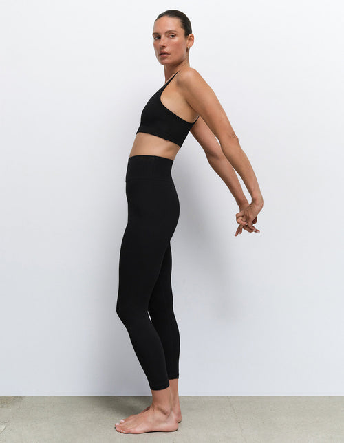 Model wearing a black sports bra and leggings from Mate the Label, stretching