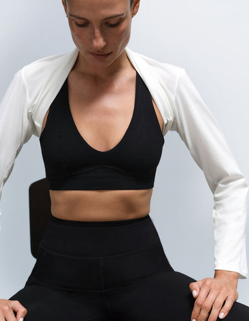 Model wearing a black sports bra and leggings from Mate the Label with a white jacket over the shoulders