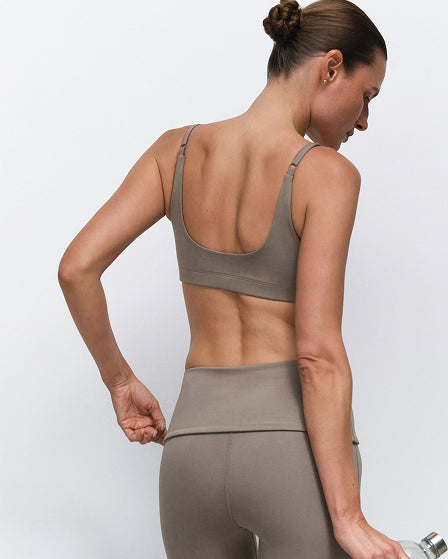Back view of a MATE model wearing a taupe activewear bra and leggings, holding a water bottle