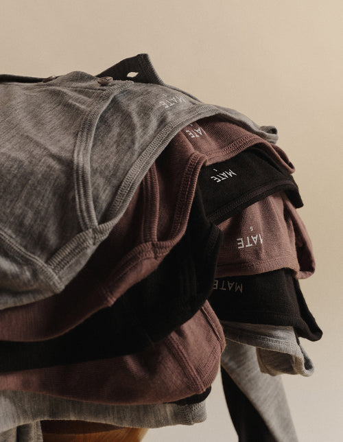 Stack of folded MATE merino wool tops in grey, brown, and black