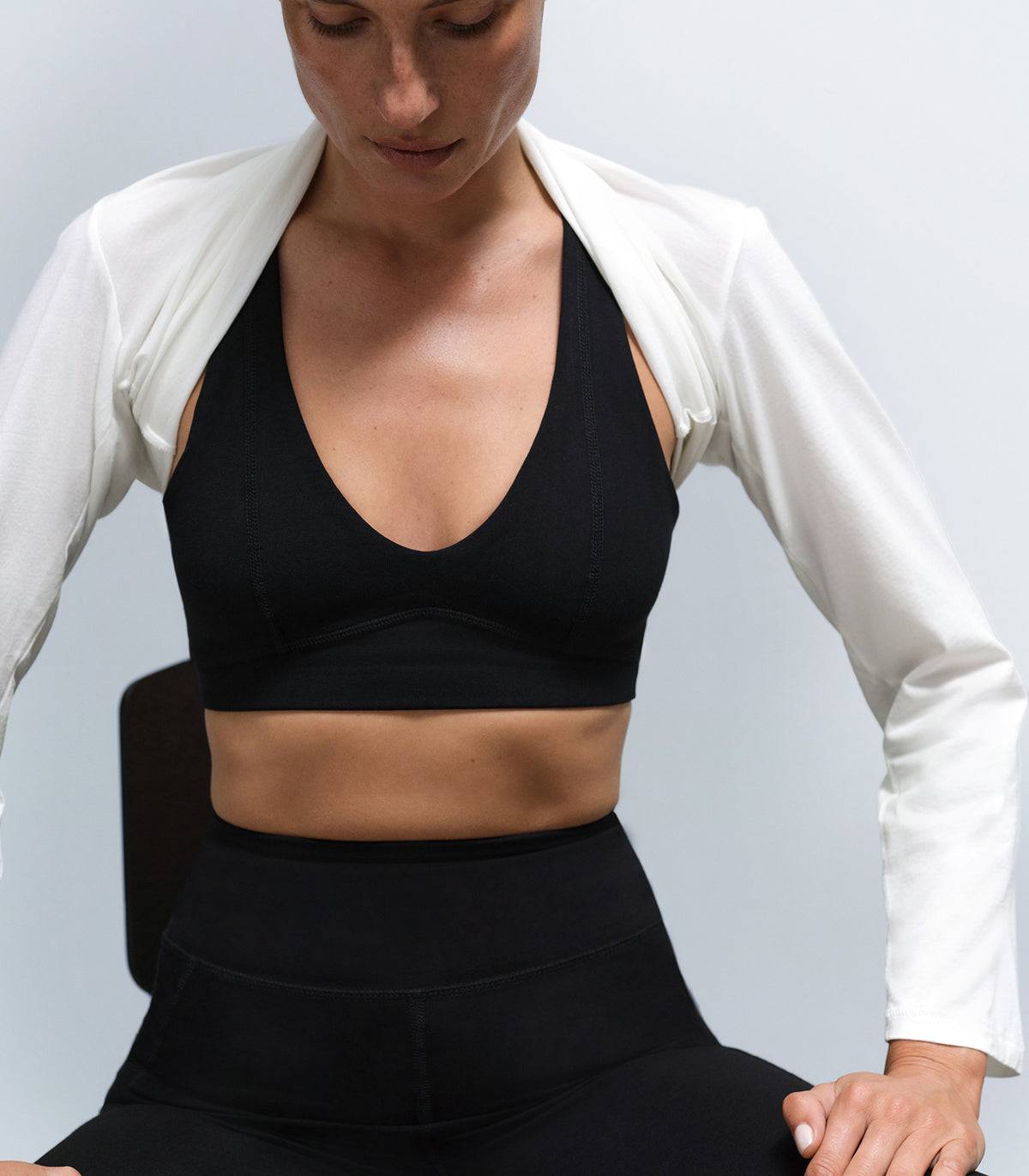 A model wearing a black halter sports bra and matching leggings with a cream cardigan draped off the shoulders
