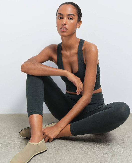 MATE model sitting cross-legged wearing a dark nori green cropped tank and matching leggings with cream slide sandals