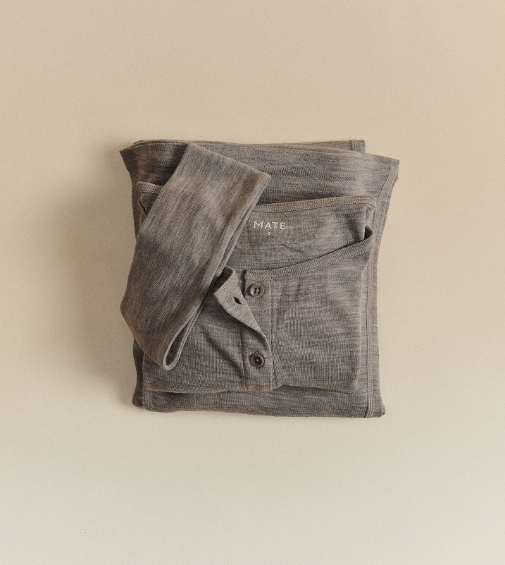 Flat lay of a folded heather grey MATE cardigan with button closures, on a beige background