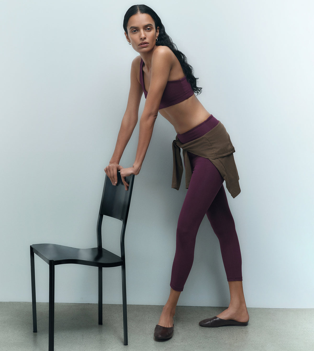 Woman in a fig organic sports bra and cropped leggings leaning on a black chair – MATE the Label