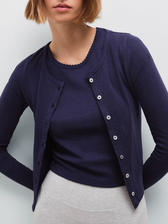 Close-up of a woman wearing a navy pointelle cardigan over a matching tank top, buttoned