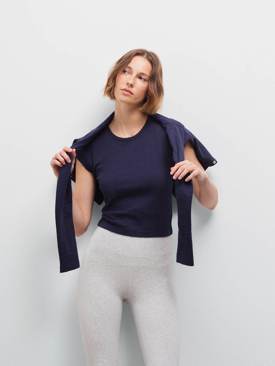 Woman holding a navy pointelle cardigan open over her shoulders, wearing a matching tank and heather grey leggings