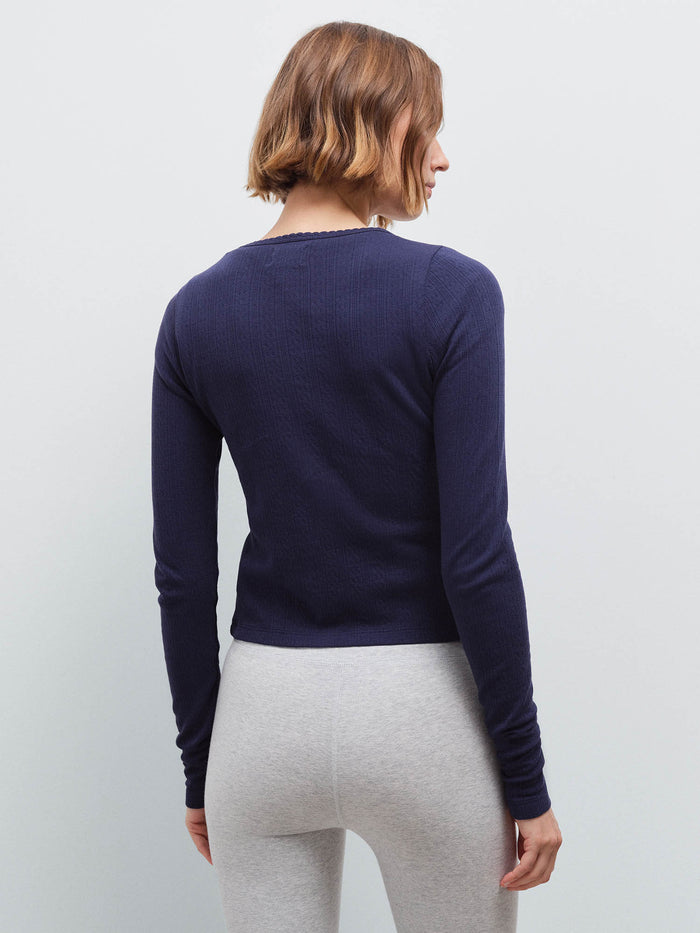 Woman standing wearing a navy pointelle cardigan and heather grey leggings, back view in studio