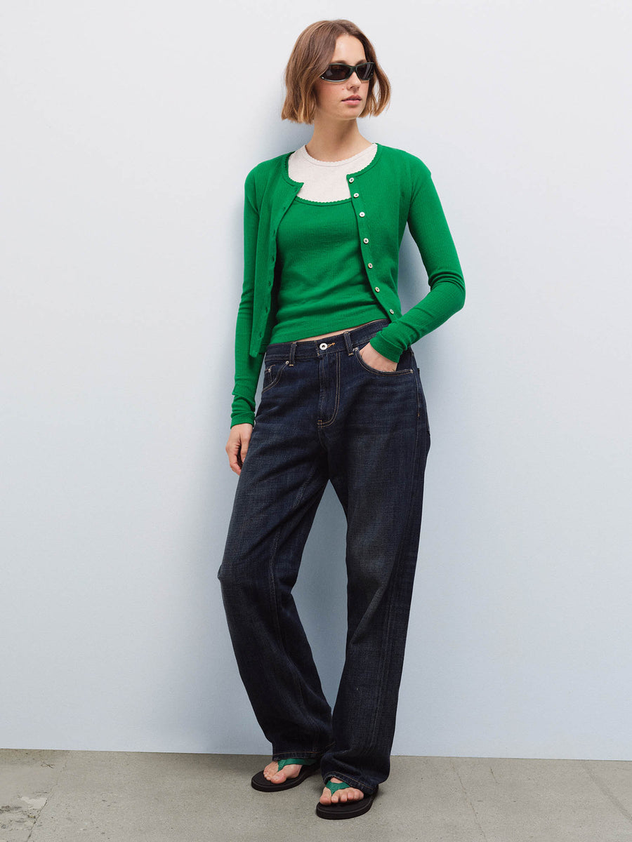 Full-length front view of a woman wearing a green pointelle cardigan and camisole with dark denim jeans and sunglasses