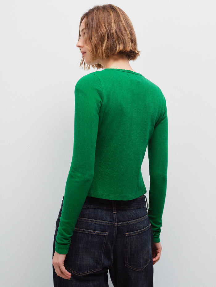Woman wearing a green pointelle cardigan and dark denim jeans, back view in studio