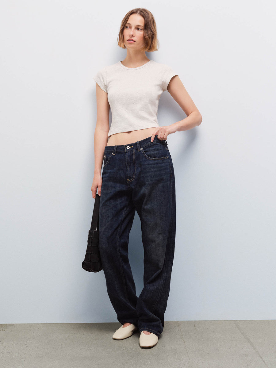 Full-length front view of a woman wearing a cream cap-sleeve baby tee and wide-leg dark denim jeans, carrying a black bag