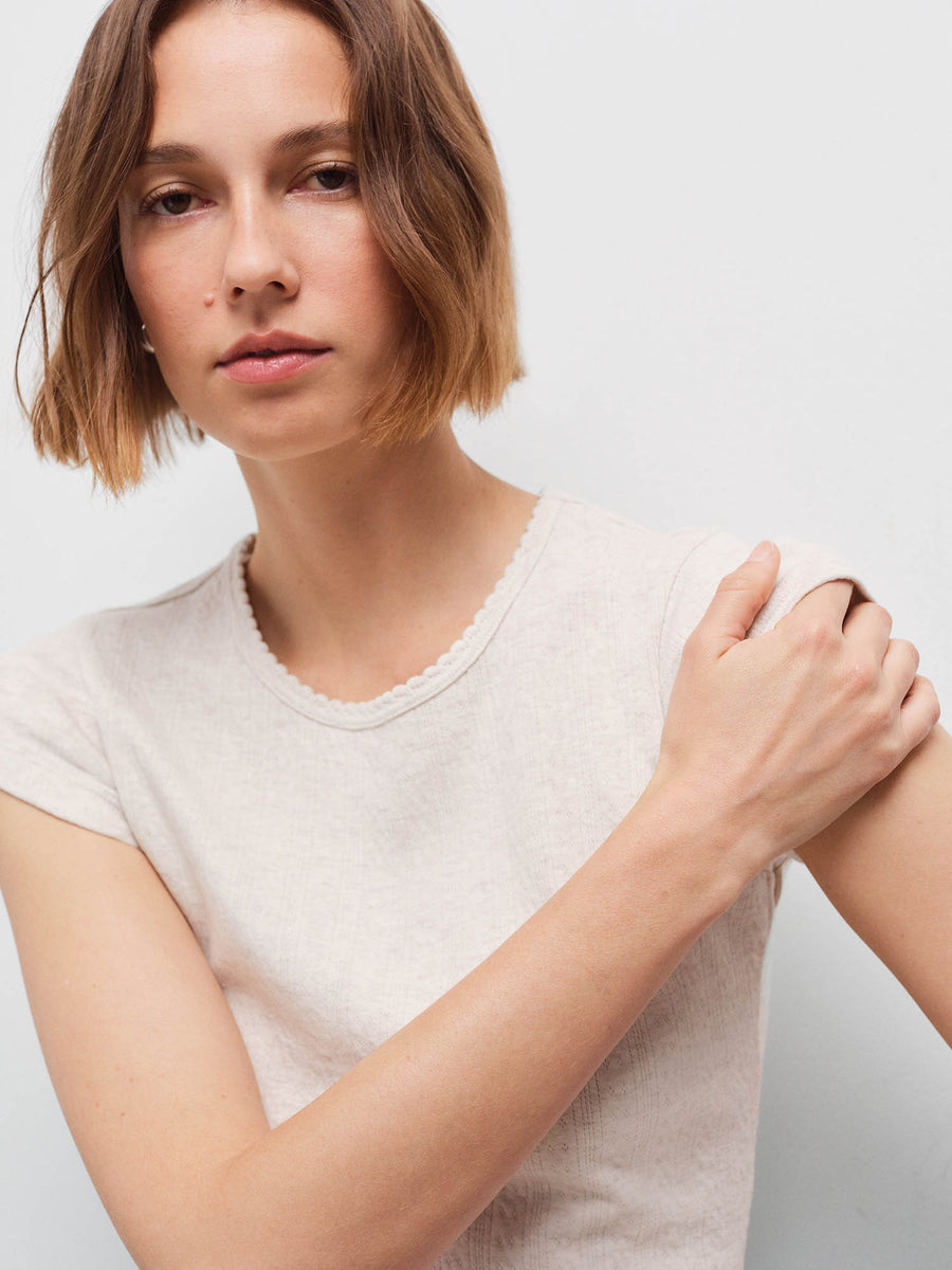 Close-up of a woman wearing a cream cap-sleeve baby tee, hand resting on her shoulder