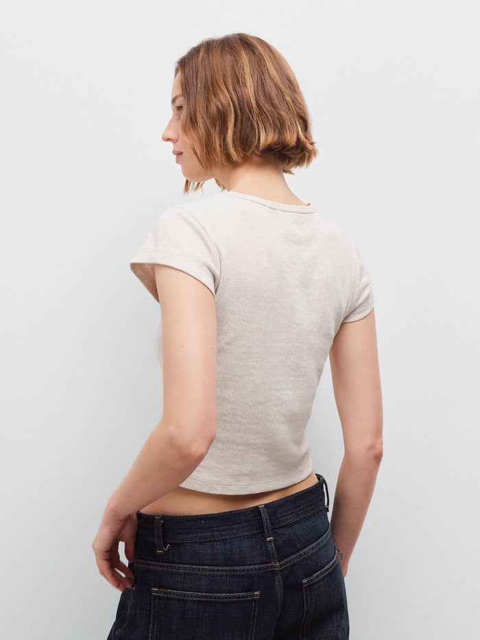 Woman standing wearing a cream cap-sleeve baby tee, back view with dark denim jeans