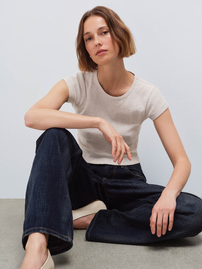 Woman seated wearing a cream cap-sleeve baby tee and dark denim jeans