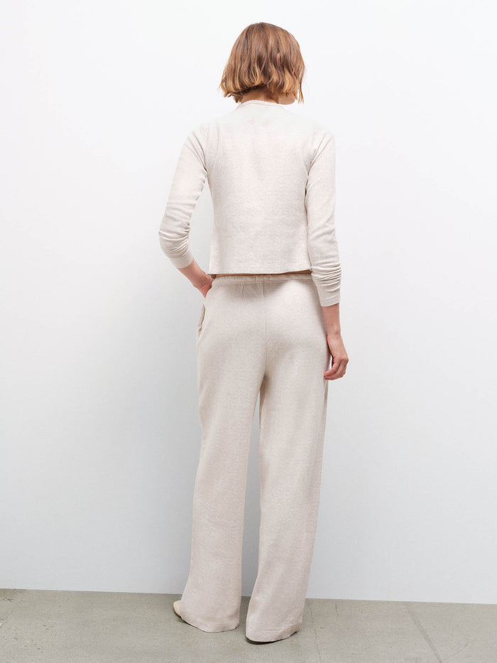 Woman standing wearing a cream pointelle top and matching wide-leg pants, back view in studio
