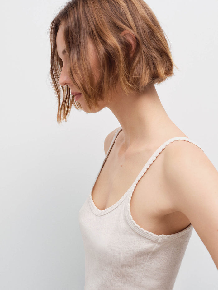 Close-up side profile of a woman wearing an oatmeal ribbed camisole with scalloped straps, studio