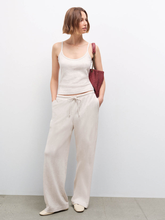 Full-length front view of a woman wearing a cream pointelle tank top and matching wide-leg pants, carrying a burgundy bag