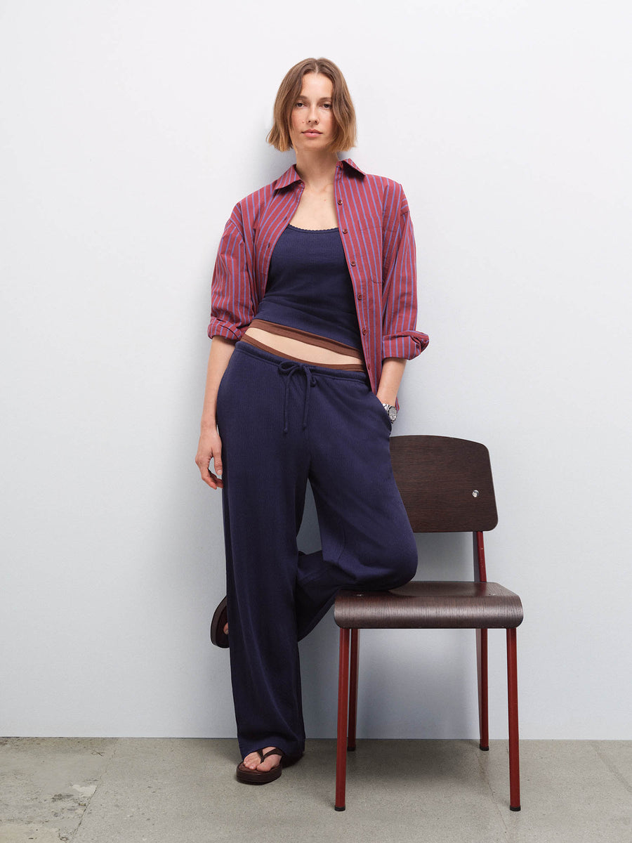 Woman wearing a red striped open shirt over a navy tank and matching pants, leaning on a chair in studio
