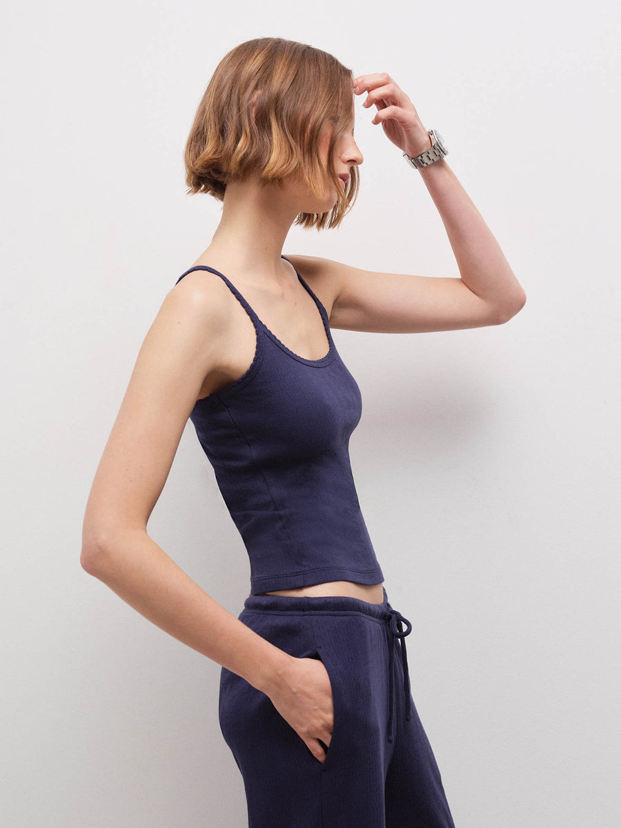 Woman wearing navy pointelle tank, side profile view with hand near forehead in studio