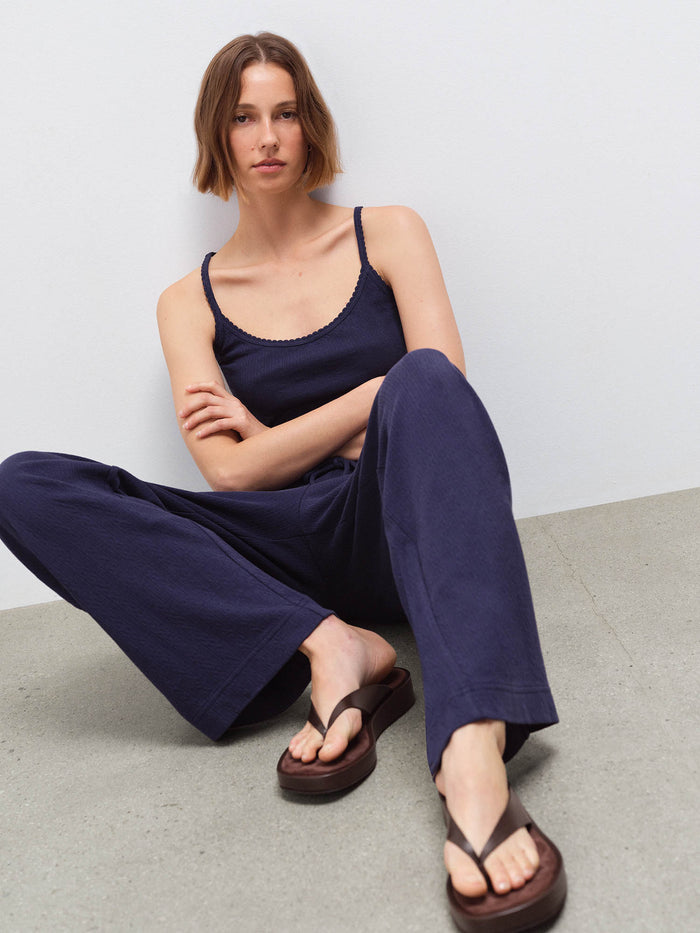 Woman seated wearing a navy pointelle scoop-neck tank top and matching wide-leg pants with brown sandals