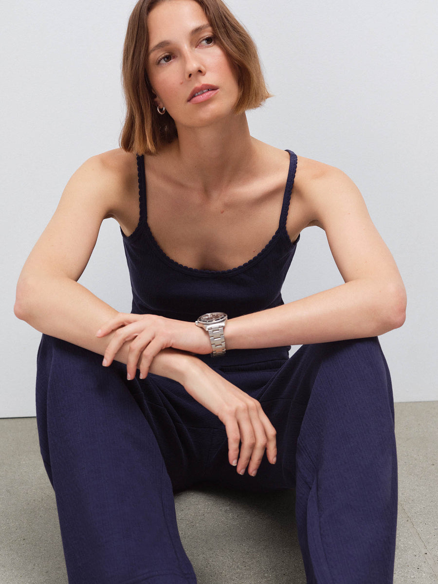 Woman wearing navy pointelle tank and pants, seated close-up with arms resting on knees in studio