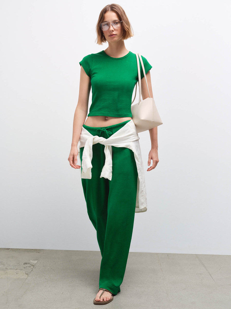 Full-body front view of a woman wearing a green cropped top and wide-leg pants with a cream cardigan tied at the waist
