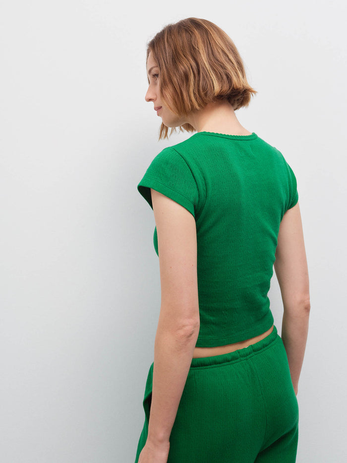 Woman standing wearing a green pointelle cap-sleeve top and matching pants, back view in studio
