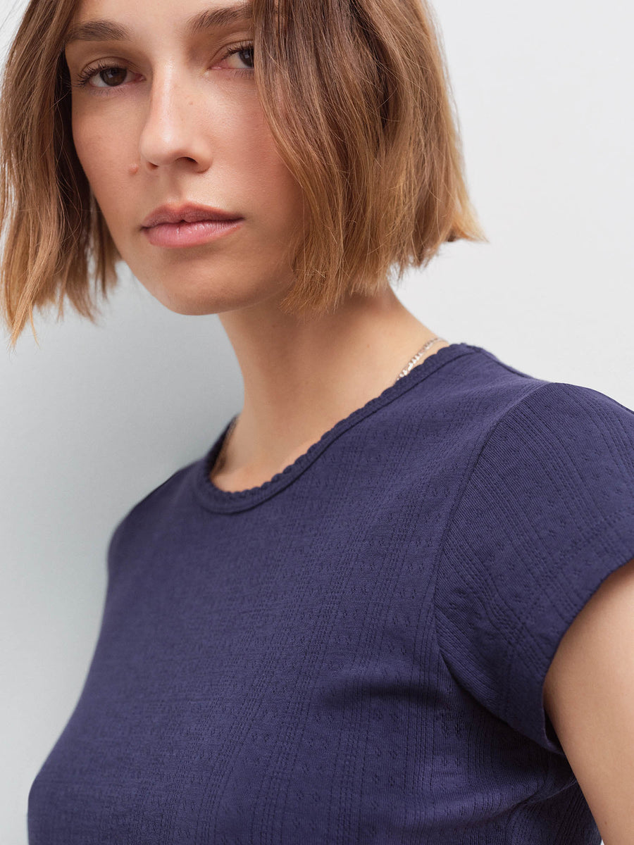 Close-up of a woman's face and shoulder wearing a navy pointelle cap-sleeve top