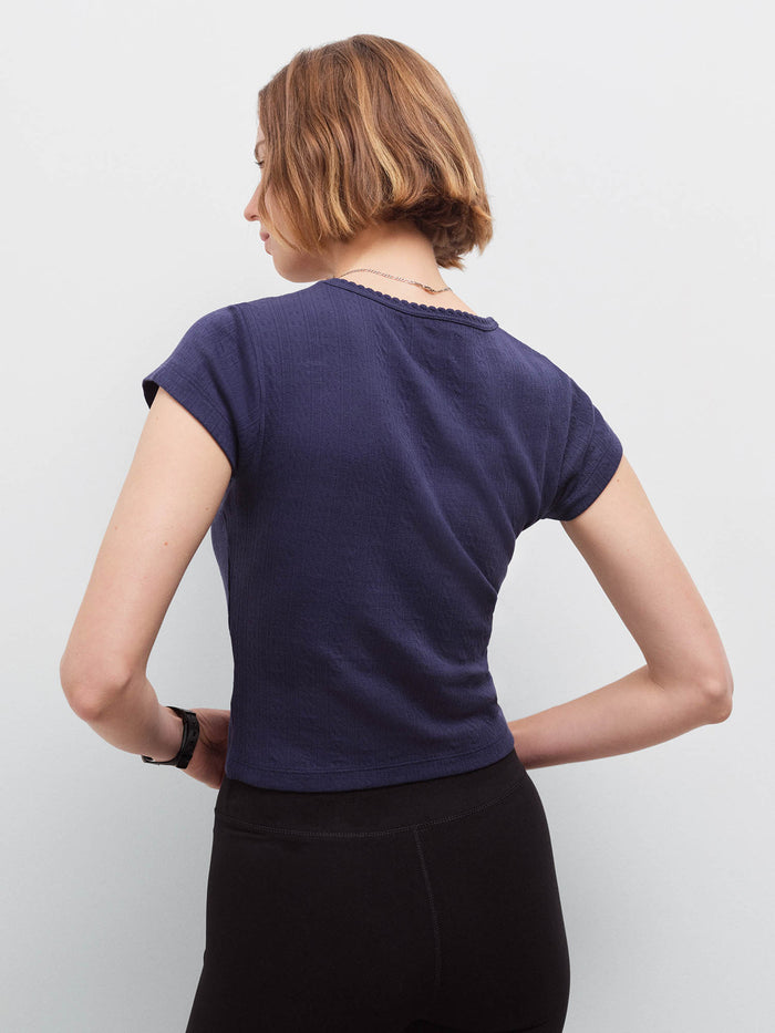 Woman wearing a navy pointelle cap-sleeve top and black shorts, back view with hands on hips