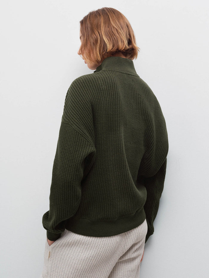 Woman wearing olive waffle-knit half-zip sweatshirt, back view showing collar and waffle texture in studio