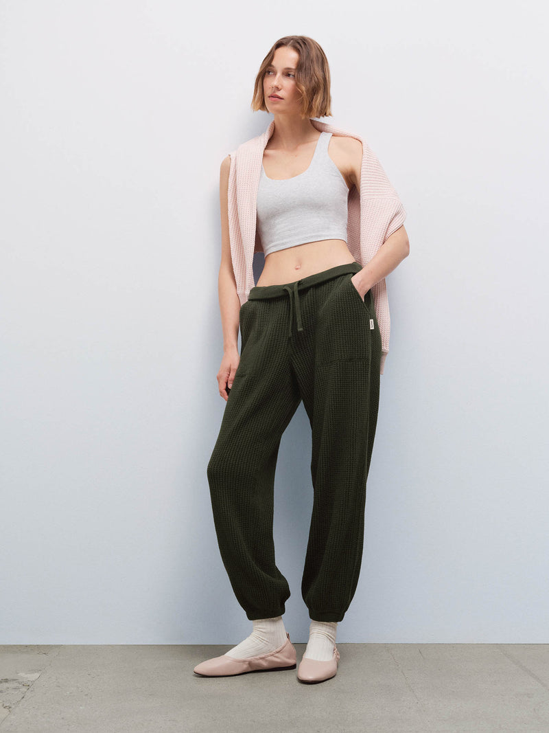 Woman wearing a heather gray cropped tank, a pink cardigan draped on her shoulders, and olive green waffle jogger sweatpants