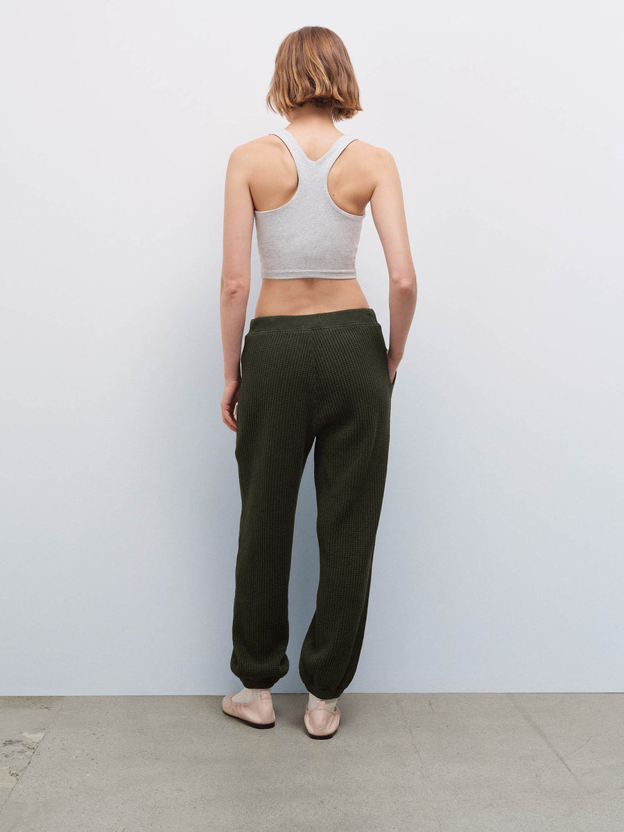 Woman wearing a heather gray racerback tank and olive green waffle-knit jogger sweatpants, back view in studio