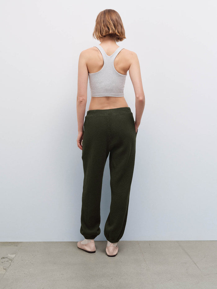 Woman wearing a heather gray racerback tank and olive green waffle-knit jogger sweatpants, back view in studio