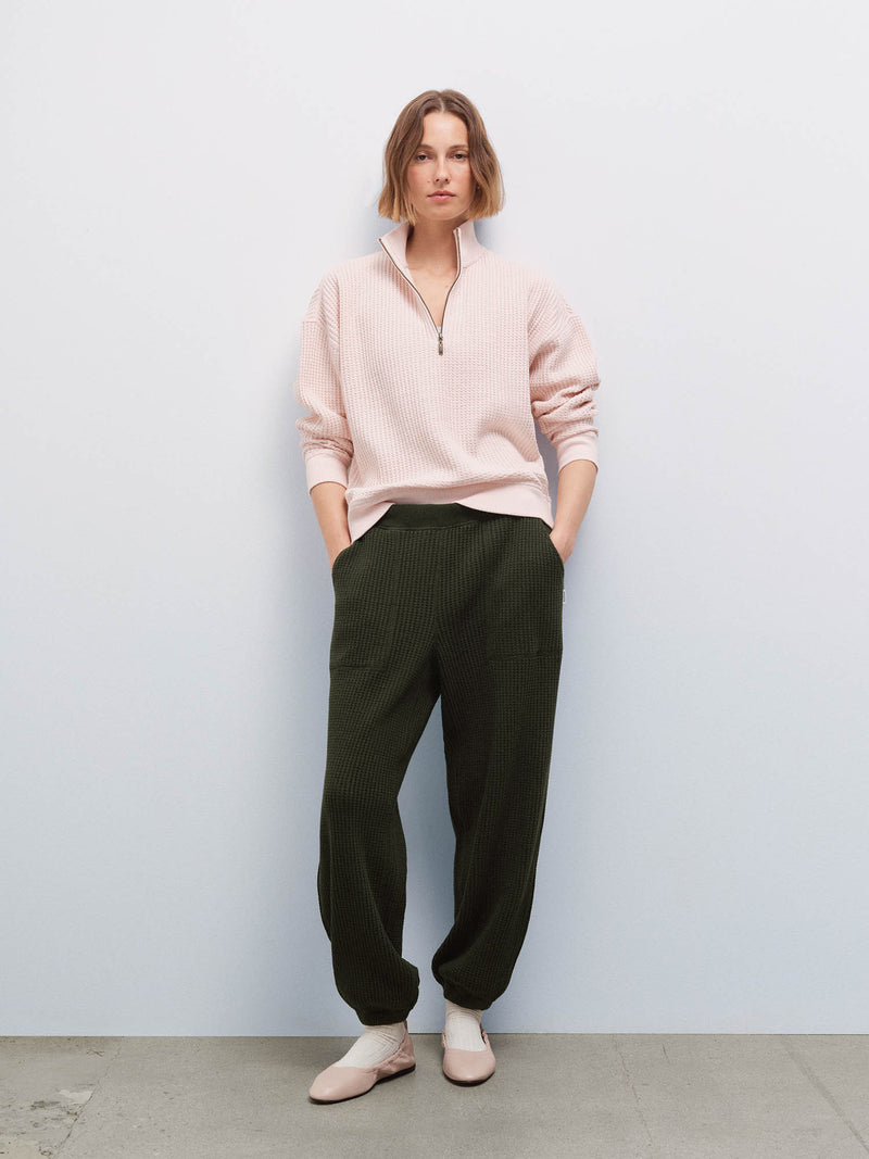 Full-body front view of a woman wearing a pale pink quarter-zip waffle pullover and olive green waffle jogger sweatpants