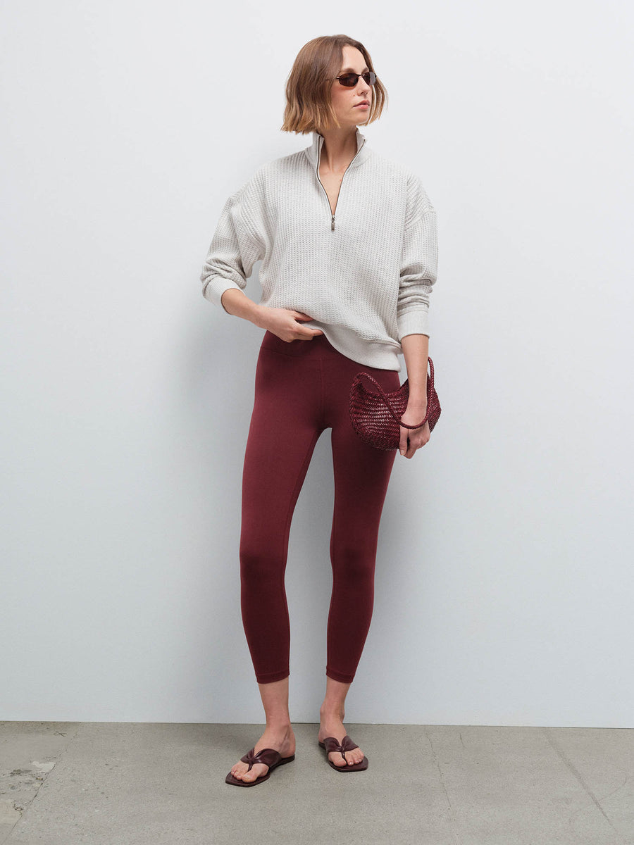 Full-length front view of a woman wearing an oversized cream waffle-knit quarter-zip pullover and burgundy leggings