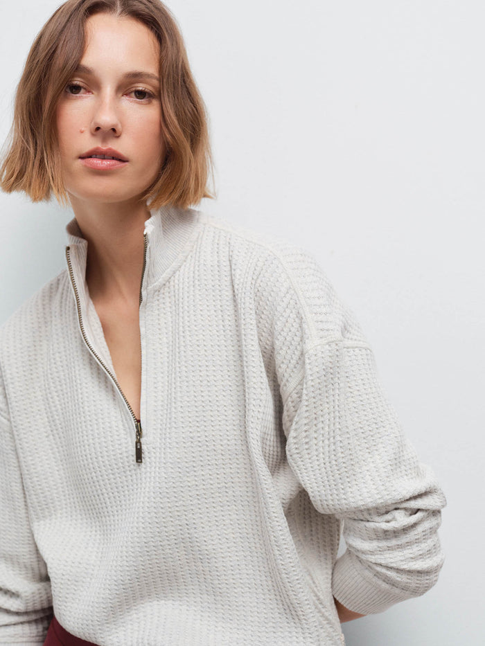 Close-up of a woman wearing a cream waffle-knit quarter-zip pullover