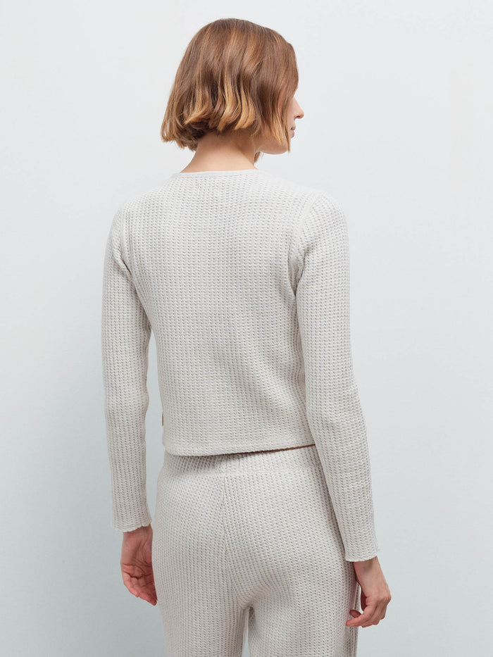 Woman wearing cream waffle-knit cardigan and matching sweatpants, back view showing knit texture in studio