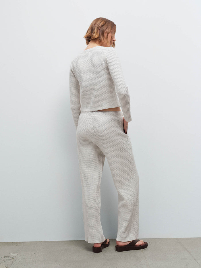 Woman standing wearing a cream marled waffle-knit cardigan and matching wide-leg pants, back view in studio