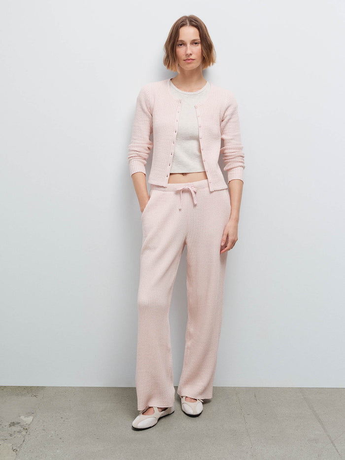 Full-length front view of a woman wearing a pale pink waffle-knit cardigan and matching wide-leg pants with white flats