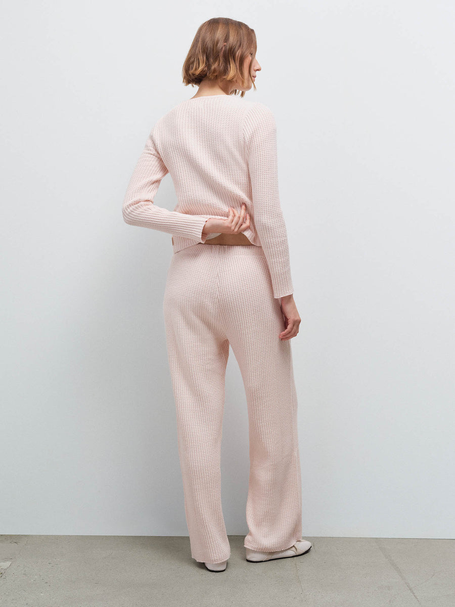 Woman standing wearing a pale pink waffle-knit cardigan and matching pants, back view in studio